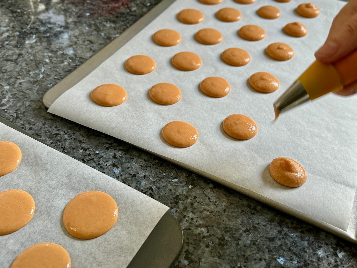 pumpkin-spiced-red-kuri-squash-macaron-filling piping out little macaron rounds on a baking sheet