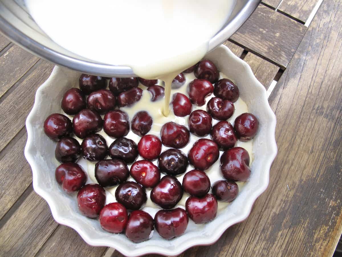 pouring clafoutis batter over whole cherries in a baking dish