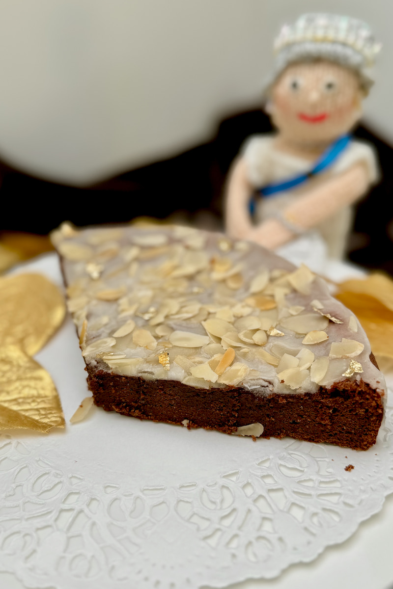 Queen of Sheba cake, a gluten-free almond flour chocolate cake topped with a rum glaze and almonds with a knitted queen looking on