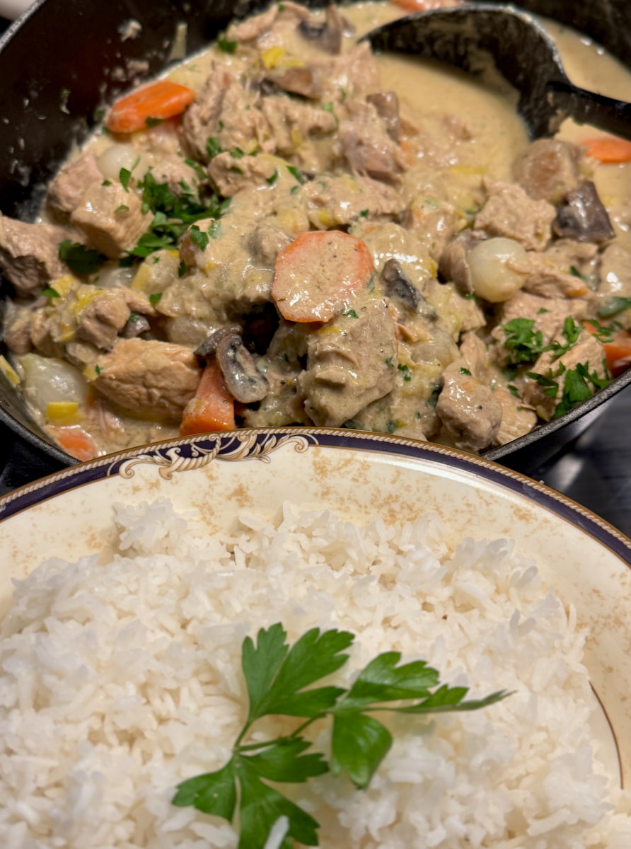 French Veal casserole in white sauce pot of French Blanquette veal stew with carrots, mushrooms and pearl onions next to a side dish of fluffy rice