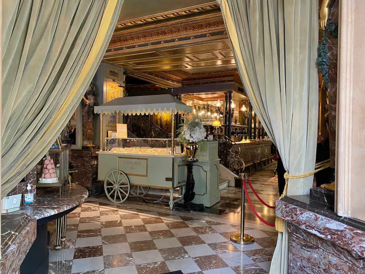 open curtains to entrance of a chic tea salon in Paris with a macaron cart