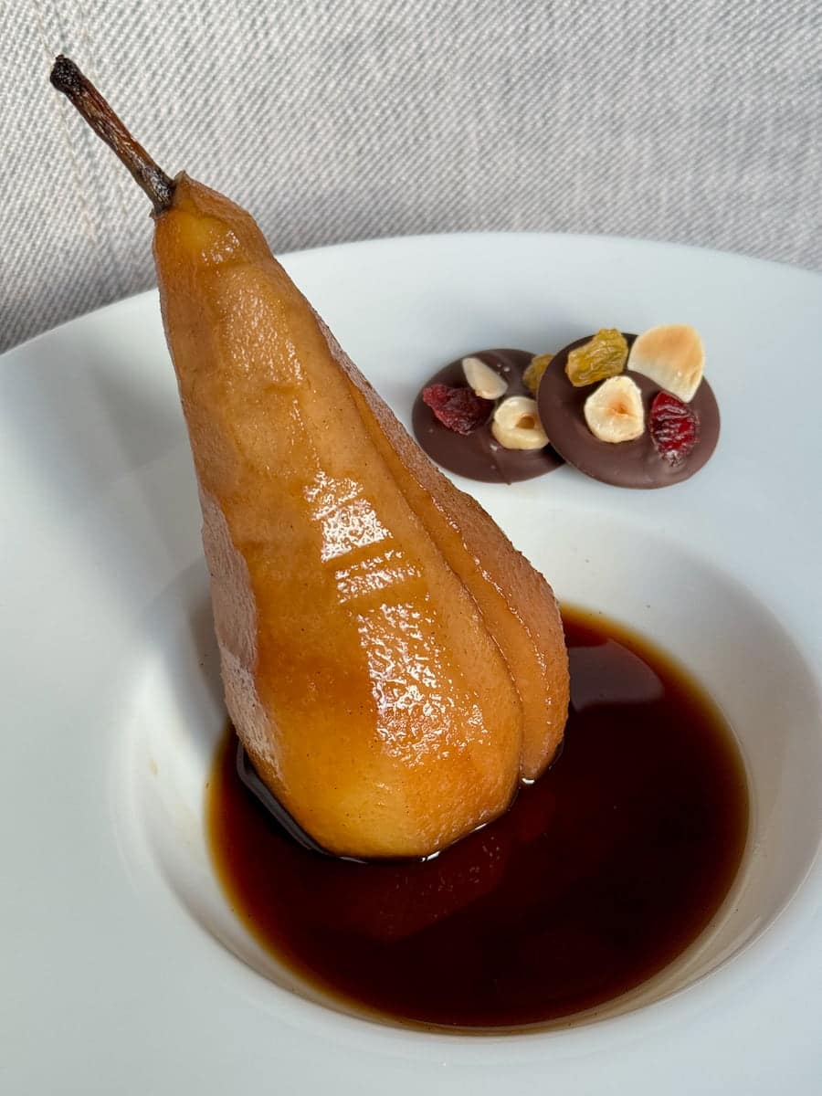 long Conference poached pear, coffee and vanilla tinted in a pool of liquid served with chocolate mendiants