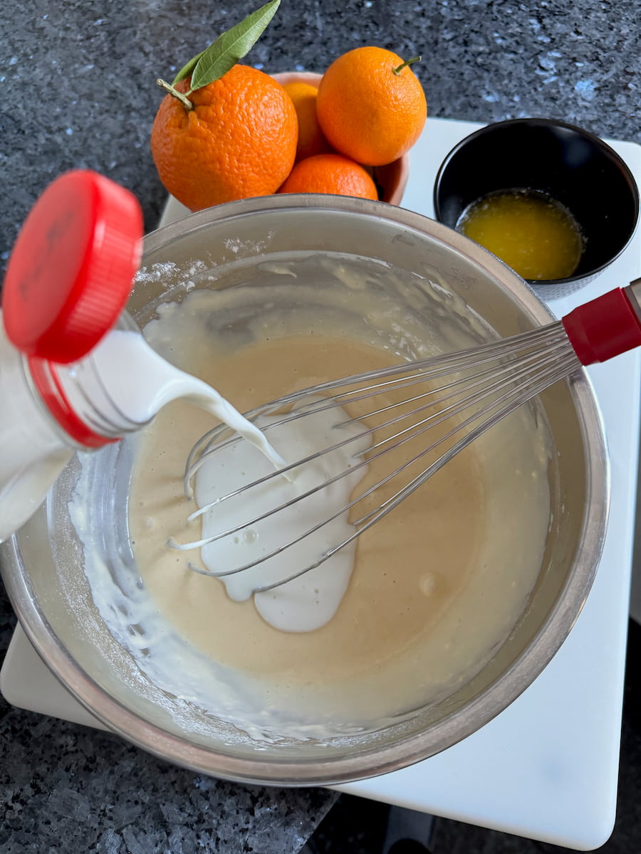 pouring whole milk into a bowl of French pancake batter without lumps