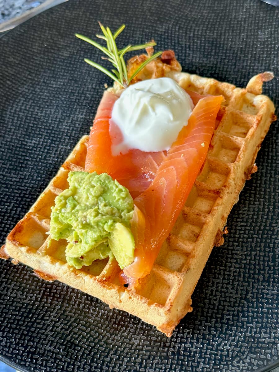 large waffle topped with smoked salmon, avocado and cream